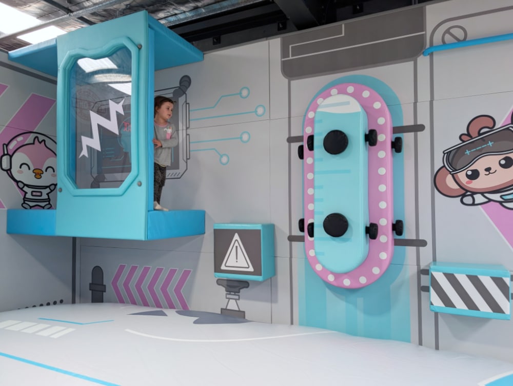 NEW Landing Play Centre Altona North 8 Child standing on a small soft-play platform next to a padded landing mat with a space-themed wall at Landing Play Centre Altona North.